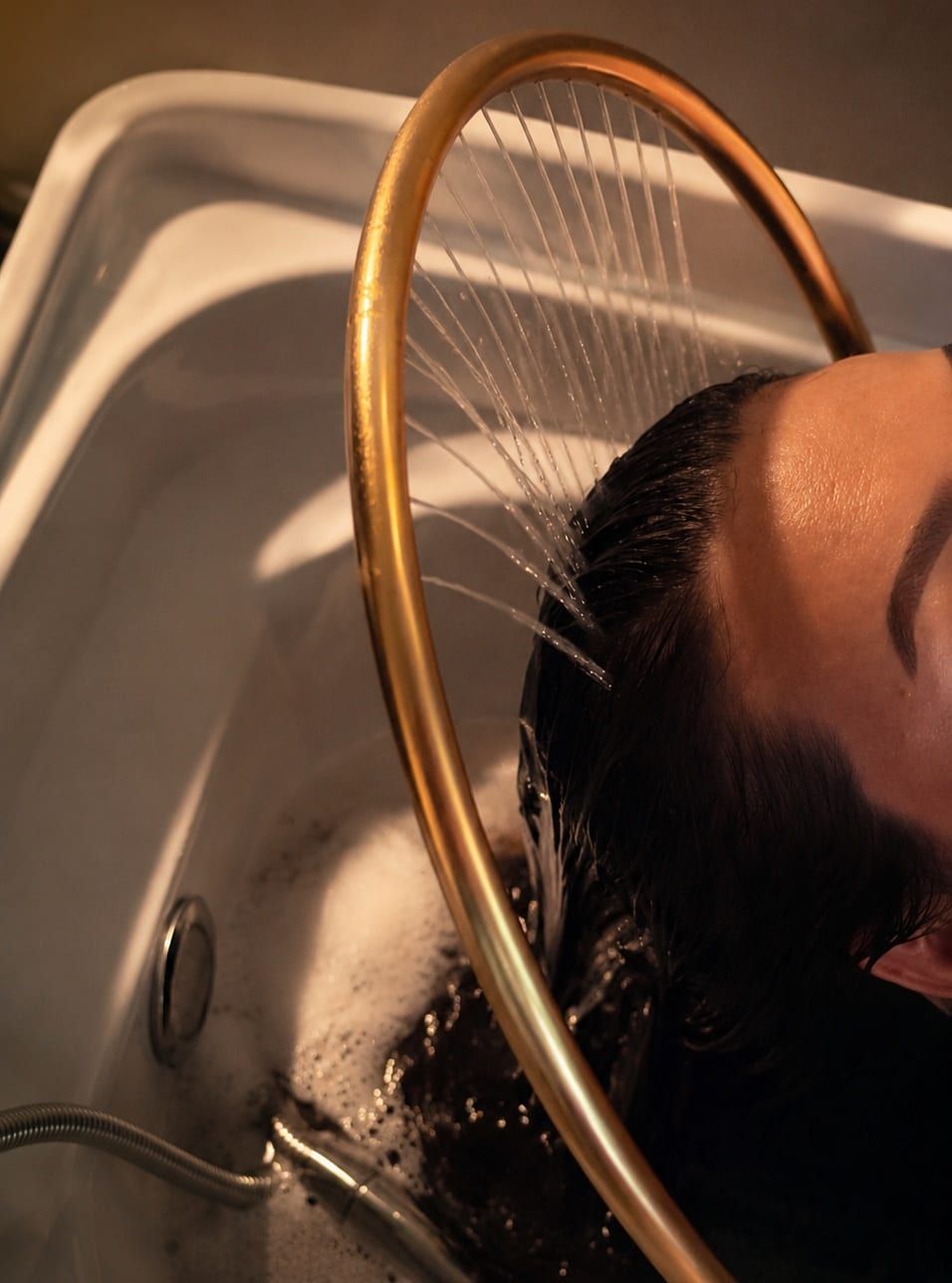 A guest having their hair rinsed under a brass spa bar during a head spa treatment at Alora in Pittsburgh