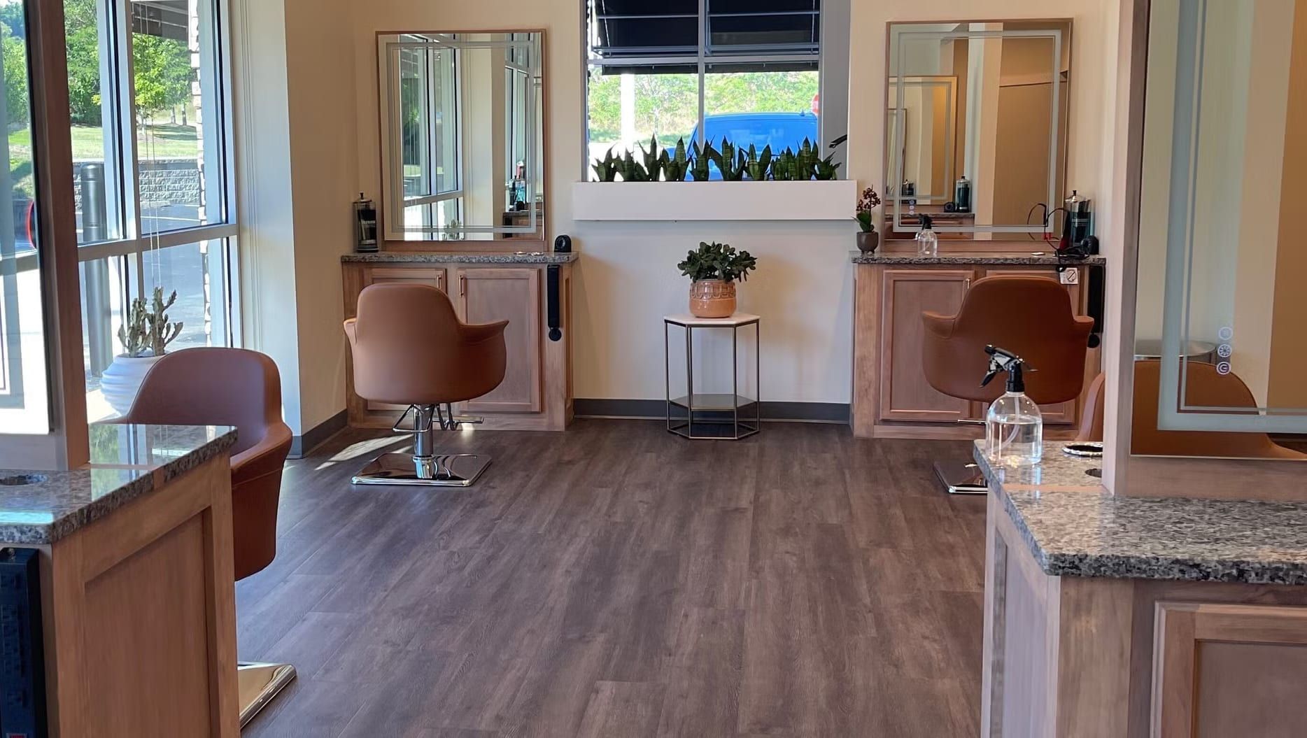 The salon floor at Alora Salon & Wellness Spa in Pittsburgh, with tan leather styling chairs, lit mirrors, plants and tall windows onto the green outside