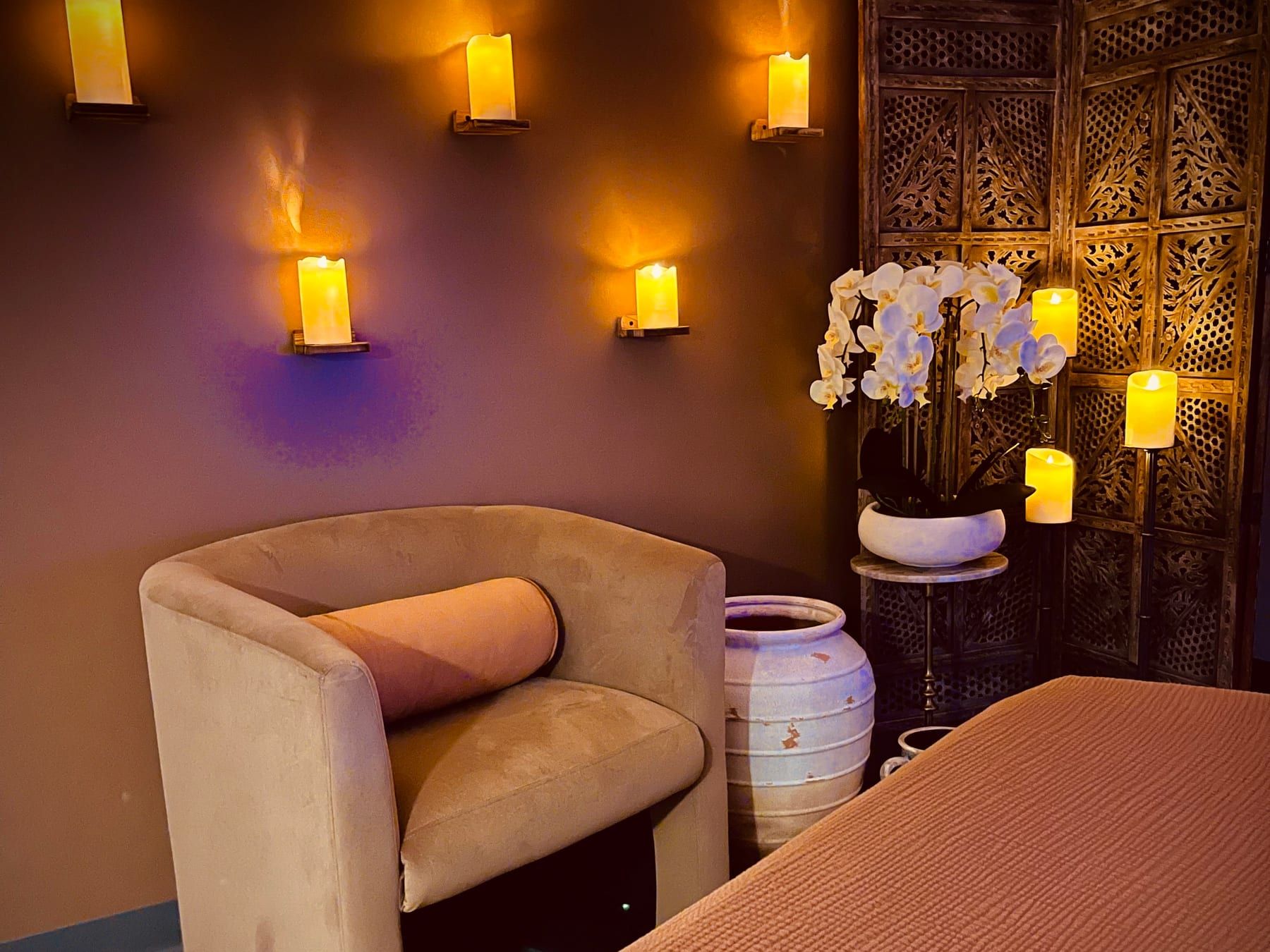 A candlelit treatment room at Alora Wellness Spa in Robinson Township, with warm wood, clay vessels and soft linen