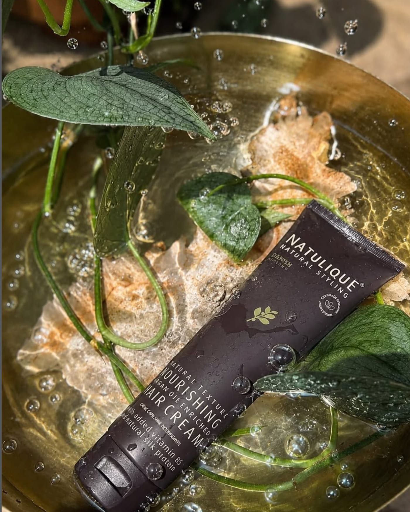 NATULIQUE Nourishing Hair Cream styled with fresh green leaves in a brass bowl of water at Alora Salon, Pittsburgh