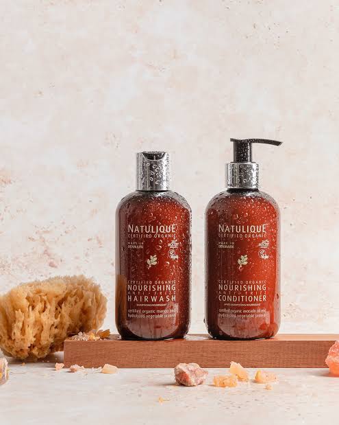 NATULIQUE certified-organic Nourishing hairwash and conditioner on a warm wooden board with a natural sponge and rose salt